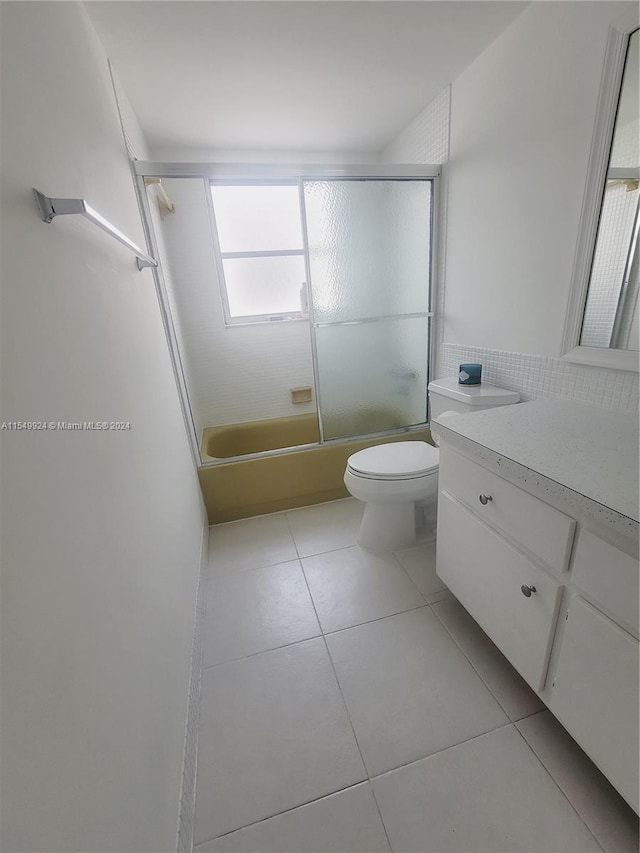 full bathroom with tile flooring, large vanity, toilet, and combined bath / shower with glass door