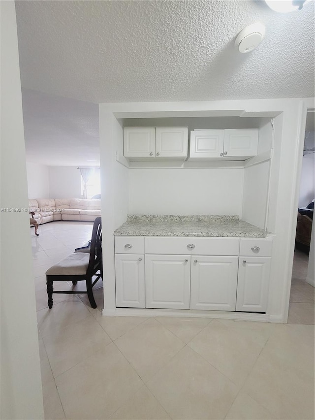 kitchen featuring light stone countertops, white cabinetry, light tile floors, and a textured ceiling