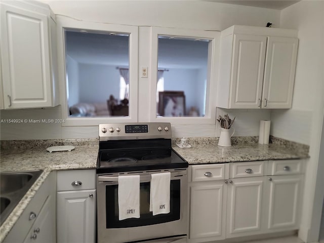 kitchen featuring stainless steel range with electric stovetop, white cabinetry, sink, and light stone counters