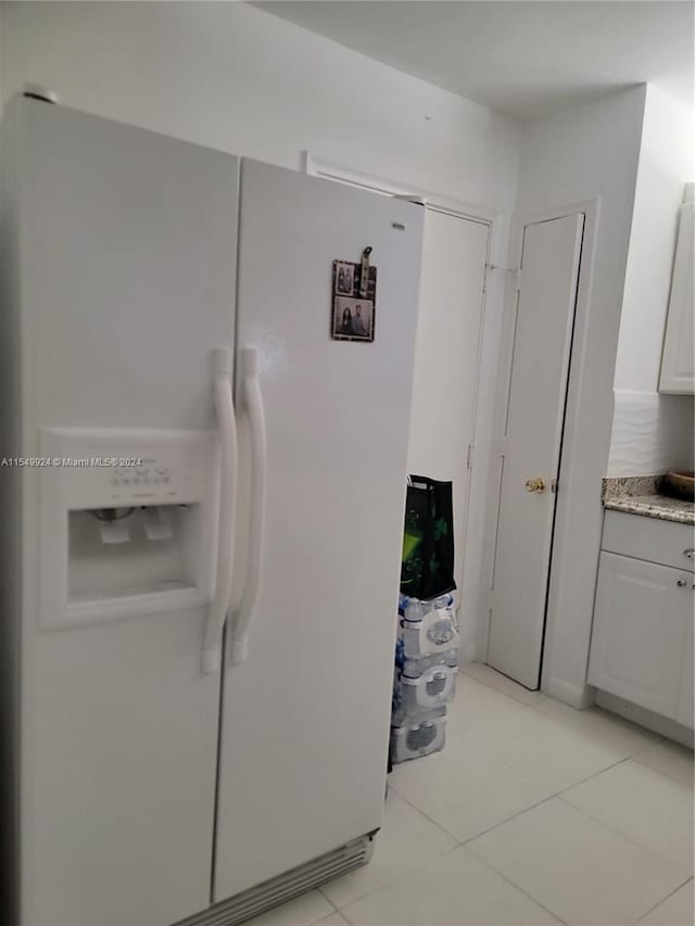 kitchen featuring white refrigerator with ice dispenser, light tile floors, and white cabinets