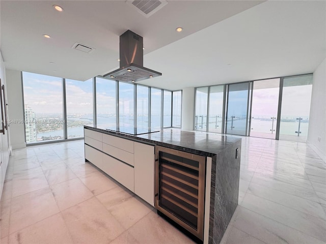 kitchen with a water view, white cabinets, beverage cooler, a center island with sink, and island exhaust hood