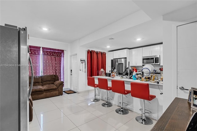 kitchen with kitchen peninsula, a breakfast bar, appliances with stainless steel finishes, light tile floors, and white cabinets