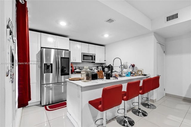 kitchen featuring a kitchen breakfast bar, light tile floors, appliances with stainless steel finishes, and white cabinetry