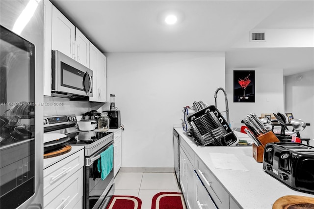 kitchen with white cabinets, light stone countertops, stainless steel appliances, and light tile floors