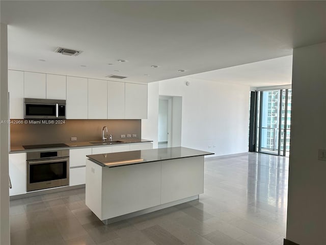 kitchen with white cabinetry, expansive windows, sink, stainless steel appliances, and a kitchen island