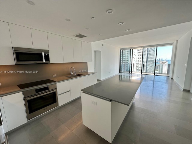 kitchen with a center island, floor to ceiling windows, appliances with stainless steel finishes, white cabinets, and sink