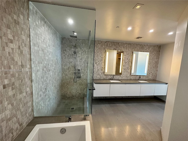 bathroom with tile walls, double vanity, hardwood / wood-style flooring, and separate shower and tub