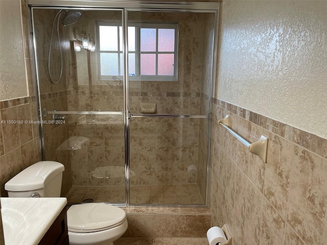 bathroom with vanity, a shower with door, toilet, and tile walls