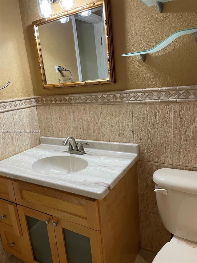 bathroom featuring vanity, toilet, and tile walls