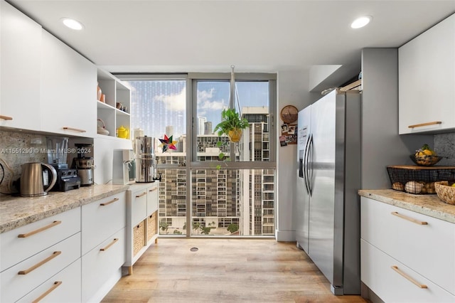 kitchen featuring white cabinets, stainless steel refrigerator with ice dispenser, plenty of natural light, and light stone counters