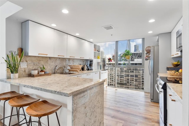 kitchen with light stone counters, white cabinetry, appliances with stainless steel finishes, sink, and light hardwood / wood-style floors