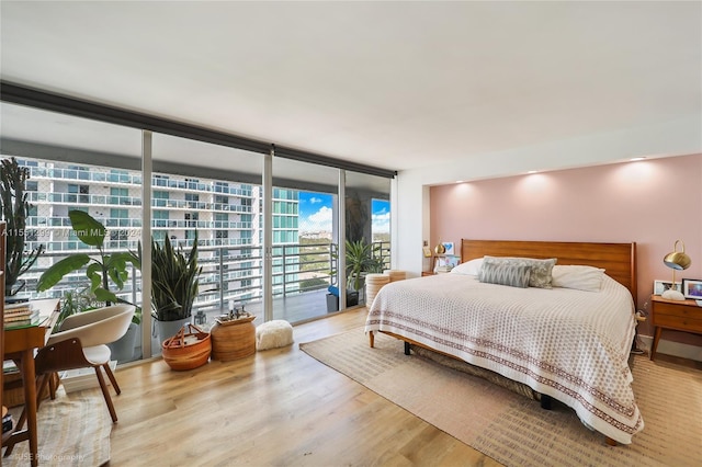 bedroom with access to exterior, light wood-type flooring, and floor to ceiling windows