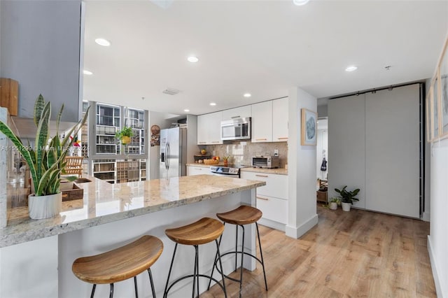 kitchen with stainless steel appliances, light hardwood / wood-style floors, kitchen peninsula, tasteful backsplash, and white cabinetry