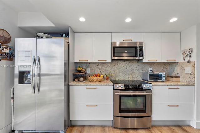 kitchen with white cabinets, light stone counters, light hardwood / wood-style flooring, and appliances with stainless steel finishes