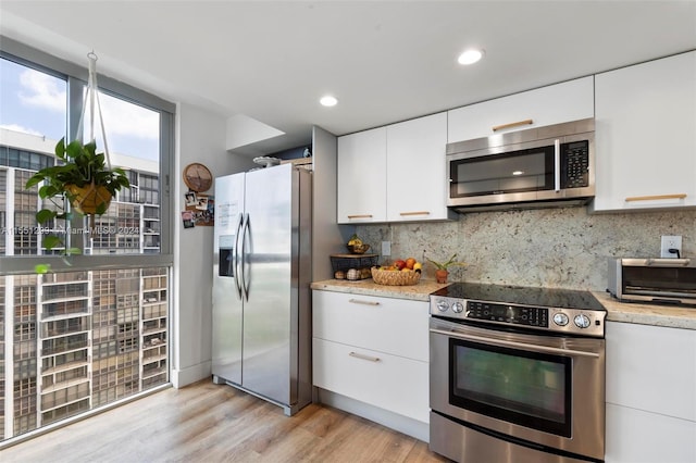 kitchen featuring tasteful backsplash, light stone counters, white cabinetry, appliances with stainless steel finishes, and light hardwood / wood-style floors