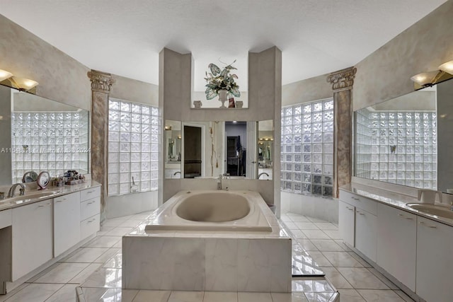 bathroom with tiled bath, dual bowl vanity, tile flooring, and a textured ceiling