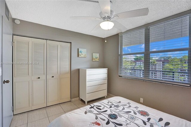 bedroom featuring a textured ceiling, a closet, a ceiling fan, visible vents, and light tile patterned flooring