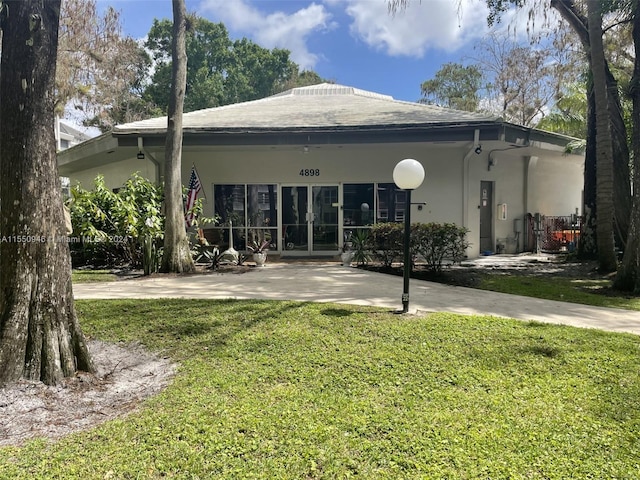 back of property with stucco siding, french doors, and a lawn