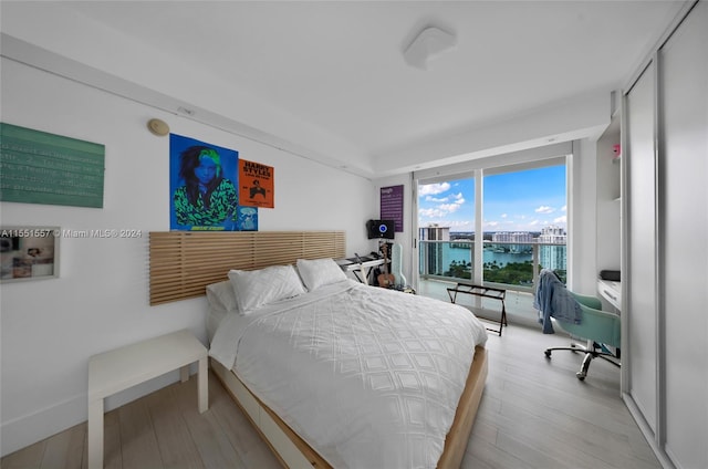 bedroom with a water view, expansive windows, and light hardwood / wood-style flooring