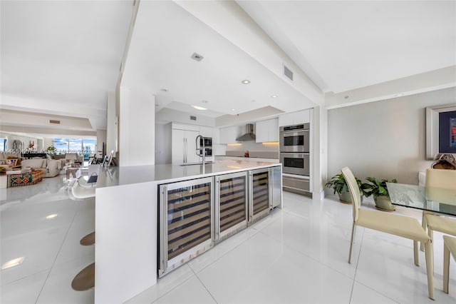 kitchen featuring wall chimney range hood, stainless steel double oven, light tile floors, and wine cooler