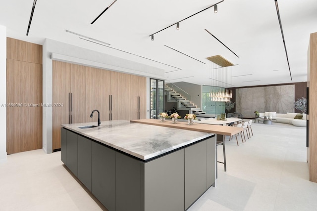 kitchen featuring sink, a kitchen breakfast bar, a large island with sink, decorative light fixtures, and gray cabinets