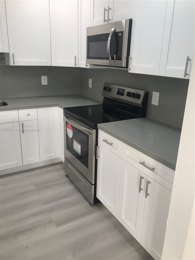 kitchen with stainless steel appliances, white cabinets, and light wood-type flooring