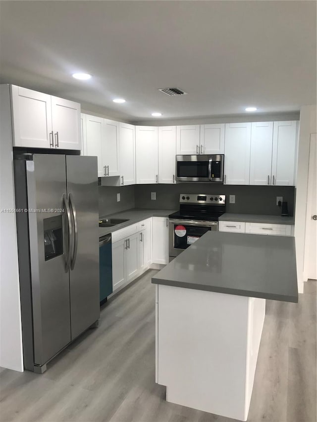 kitchen featuring light hardwood / wood-style floors, a kitchen island, white cabinets, sink, and appliances with stainless steel finishes