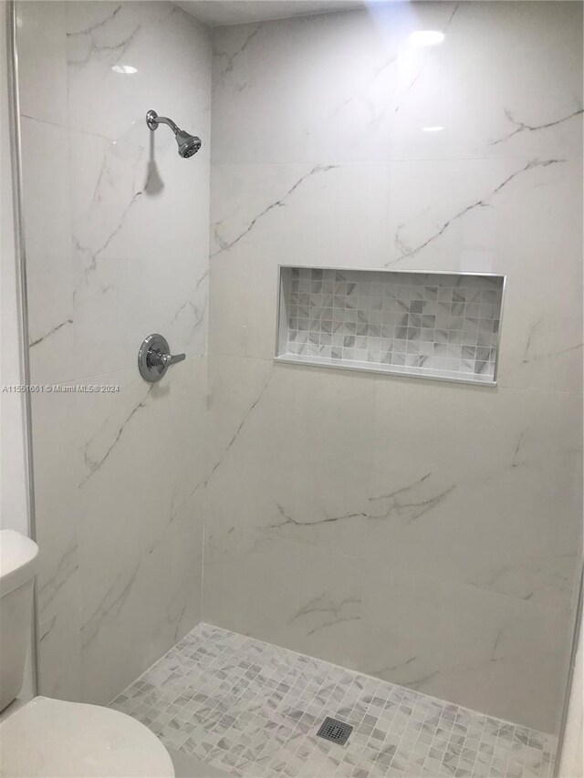 bathroom with a tile shower and toilet