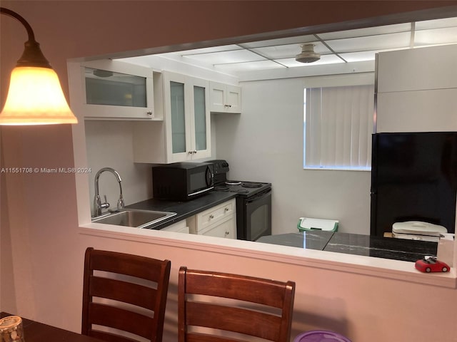 kitchen with a drop ceiling, sink, white cabinets, and black appliances