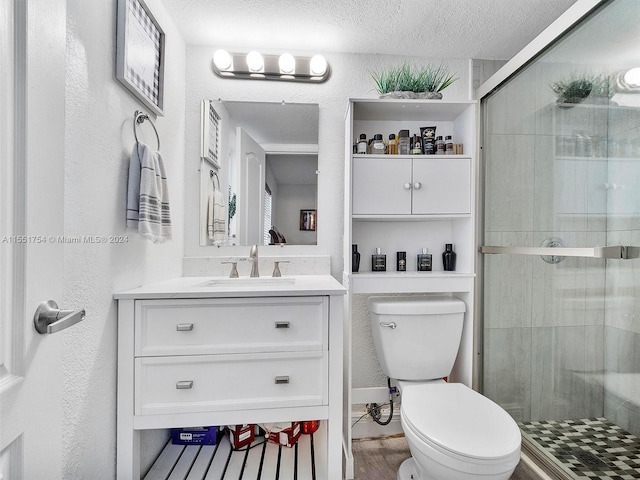 bathroom with a textured ceiling, vanity, walk in shower, and toilet