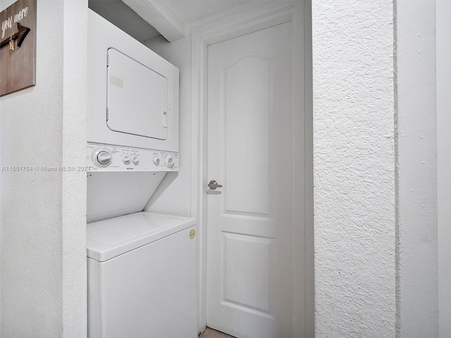 clothes washing area featuring stacked washer / dryer, laundry area, and a textured wall