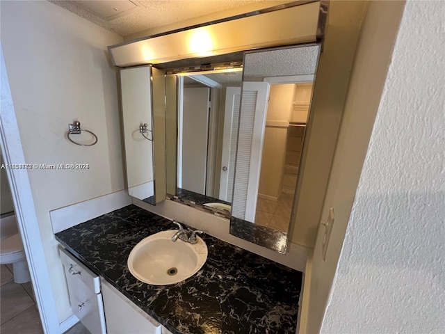 bathroom featuring toilet, a textured ceiling, vanity with extensive cabinet space, and tile flooring