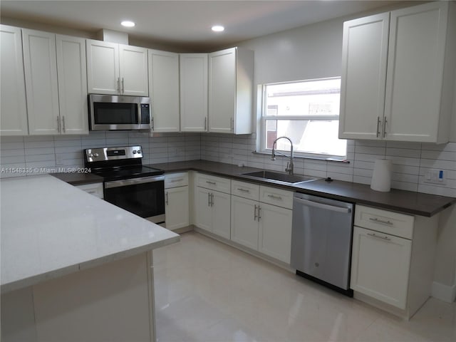 kitchen featuring white cabinetry, appliances with stainless steel finishes, sink, light tile floors, and tasteful backsplash