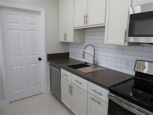 kitchen with white cabinetry, backsplash, sink, stainless steel appliances, and light tile floors