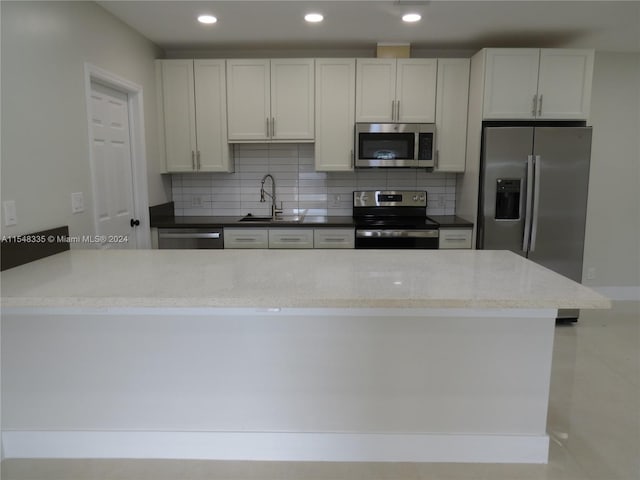 kitchen with stainless steel appliances, dark stone counters, white cabinets, backsplash, and sink