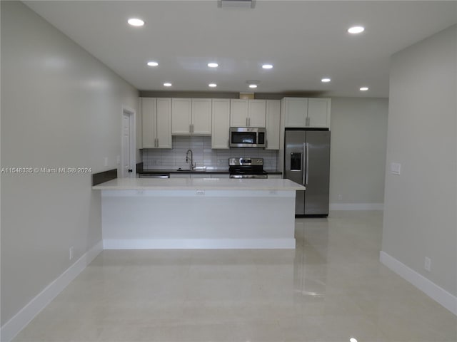 kitchen featuring kitchen peninsula, appliances with stainless steel finishes, white cabinets, backsplash, and sink