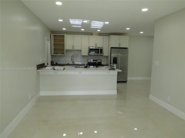 kitchen with kitchen peninsula, white cabinetry, backsplash, and stainless steel appliances