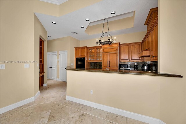 kitchen with a raised ceiling, kitchen peninsula, paneled built in refrigerator, decorative light fixtures, and black oven