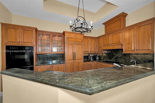 kitchen featuring kitchen peninsula, backsplash, a raised ceiling, an inviting chandelier, and hanging light fixtures