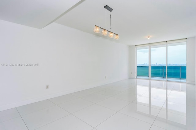 unfurnished room with floor to ceiling windows, a water view, and light tile floors