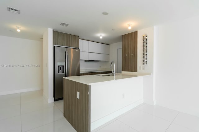 kitchen featuring sink, stainless steel fridge, light tile flooring, and white cabinetry