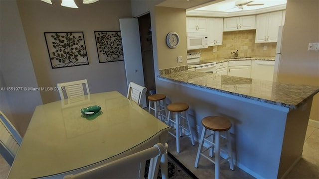 kitchen with sink, white cabinets, a kitchen bar, kitchen peninsula, and white appliances