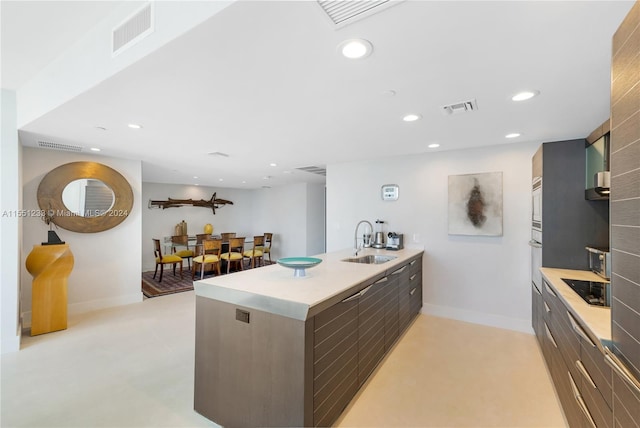 kitchen with stovetop, a kitchen island with sink, sink, and stainless steel oven