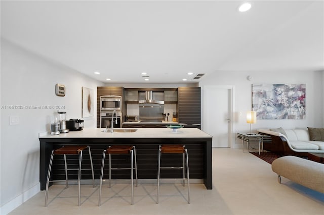 kitchen with kitchen peninsula, sink, stainless steel appliances, wall chimney exhaust hood, and a kitchen bar