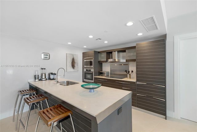 kitchen featuring appliances with stainless steel finishes, sink, light tile floors, wall chimney range hood, and a breakfast bar area