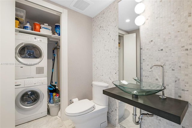 bathroom with stacked washer / drying machine, toilet, and tile floors