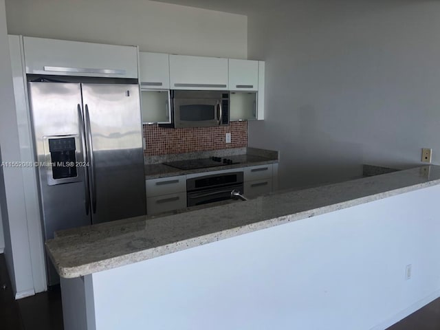 kitchen with tasteful backsplash, stainless steel appliances, white cabinetry, and light stone counters