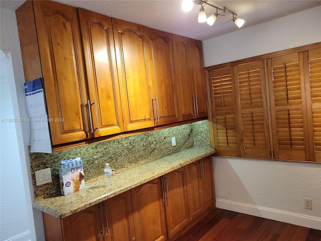 kitchen featuring decorative backsplash, dark hardwood / wood-style floors, track lighting, and light stone counters