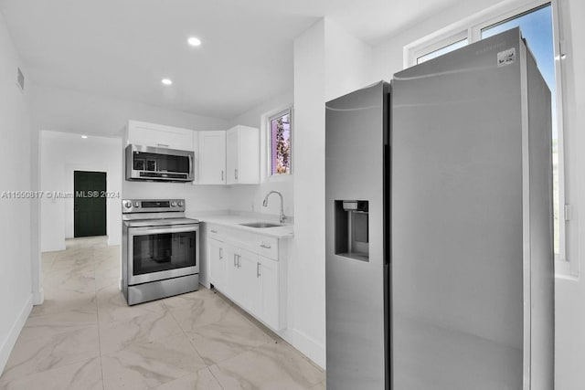 kitchen featuring stainless steel appliances, light tile flooring, white cabinets, a healthy amount of sunlight, and sink