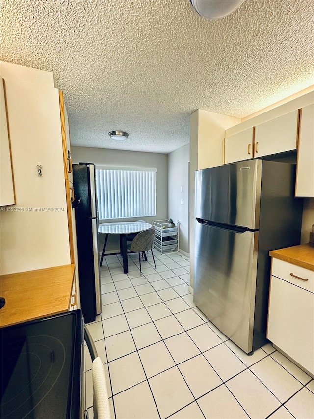 kitchen featuring range, light tile patterned floors, a textured ceiling, and stainless steel refrigerator